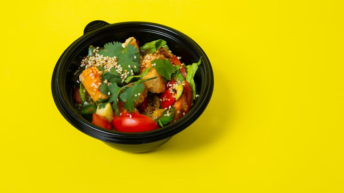 From above of delicious healthy salad consisting of various vegetables in plastic bowl placed on bright yellow background